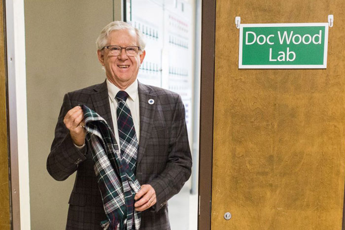 Professor Emeritus Hugh Wood standing in front of a door with a sign that reads Doc Wood Lab